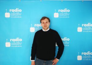 Geschäftsführer Jan Waitzmann vor einer Wand mit dem Logo von Radio-Aktiv